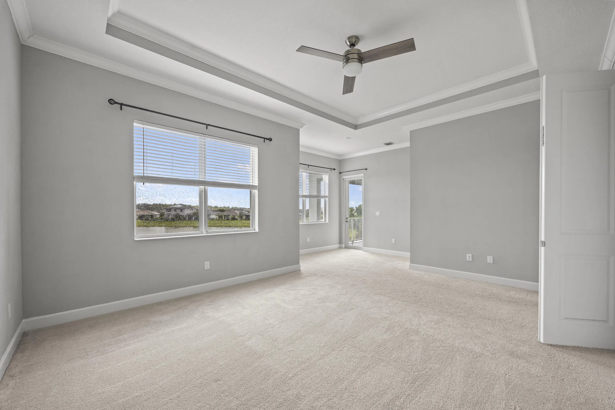 Expansive room with neutral carpeting, tray ceiling, and ceiling fan