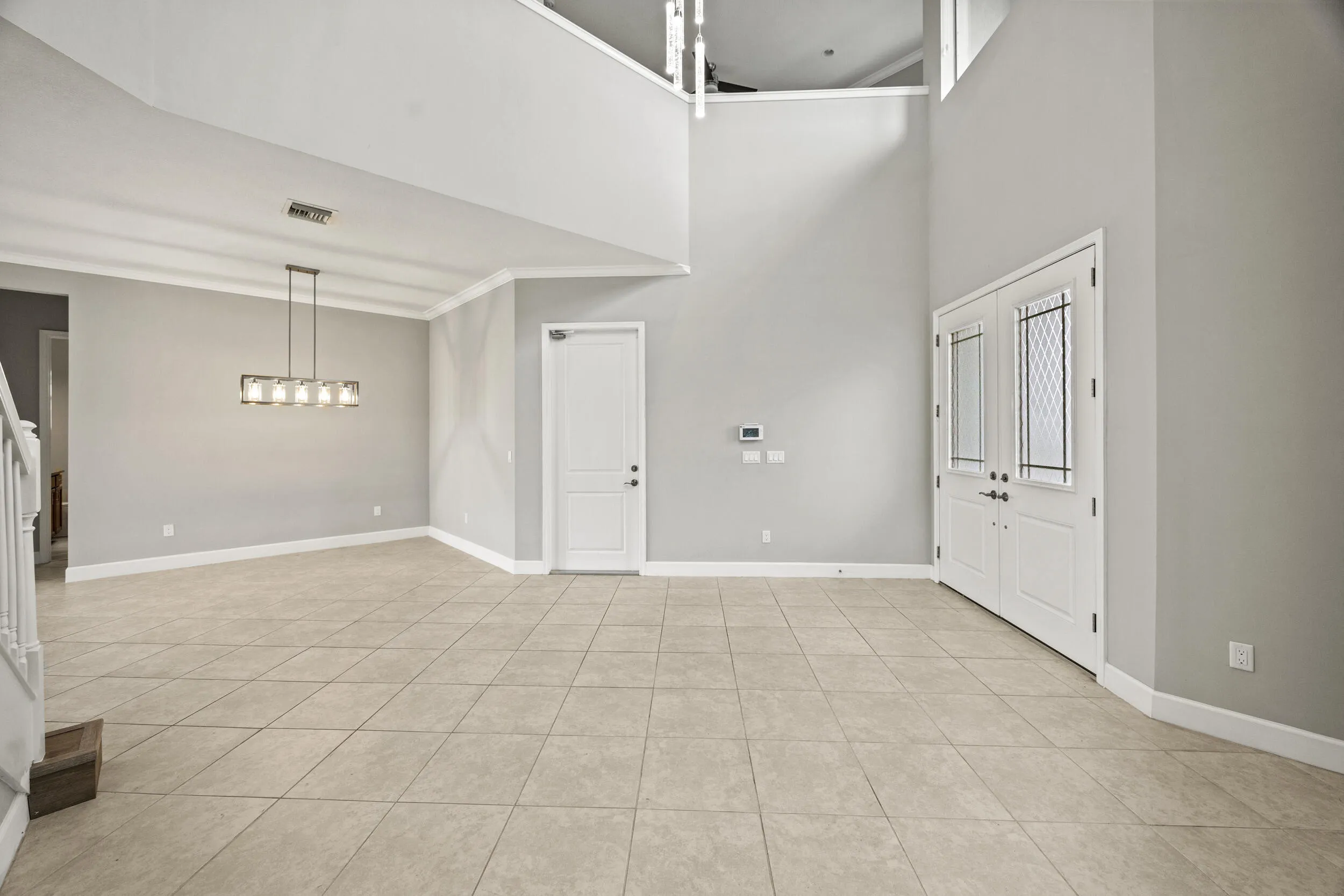 Two-story foyer with a double-door entry, tiled flooring, and a linear chandelier