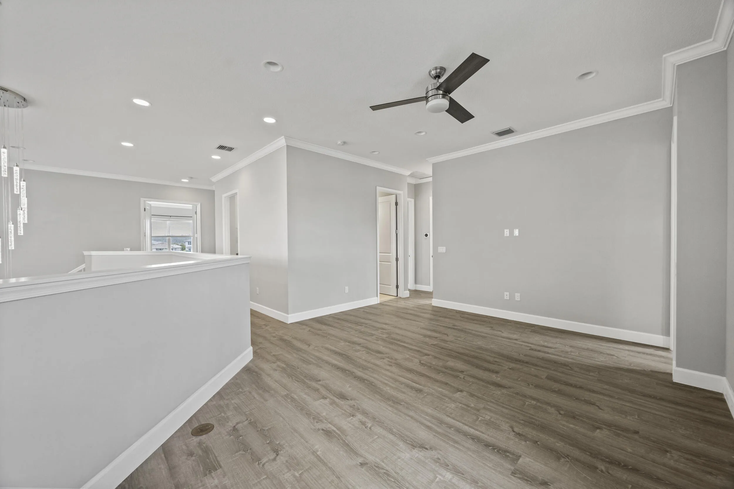 Wood-finish flooring, recessed lighting, ceiling fan, crown molding, and a contemporary chandelier