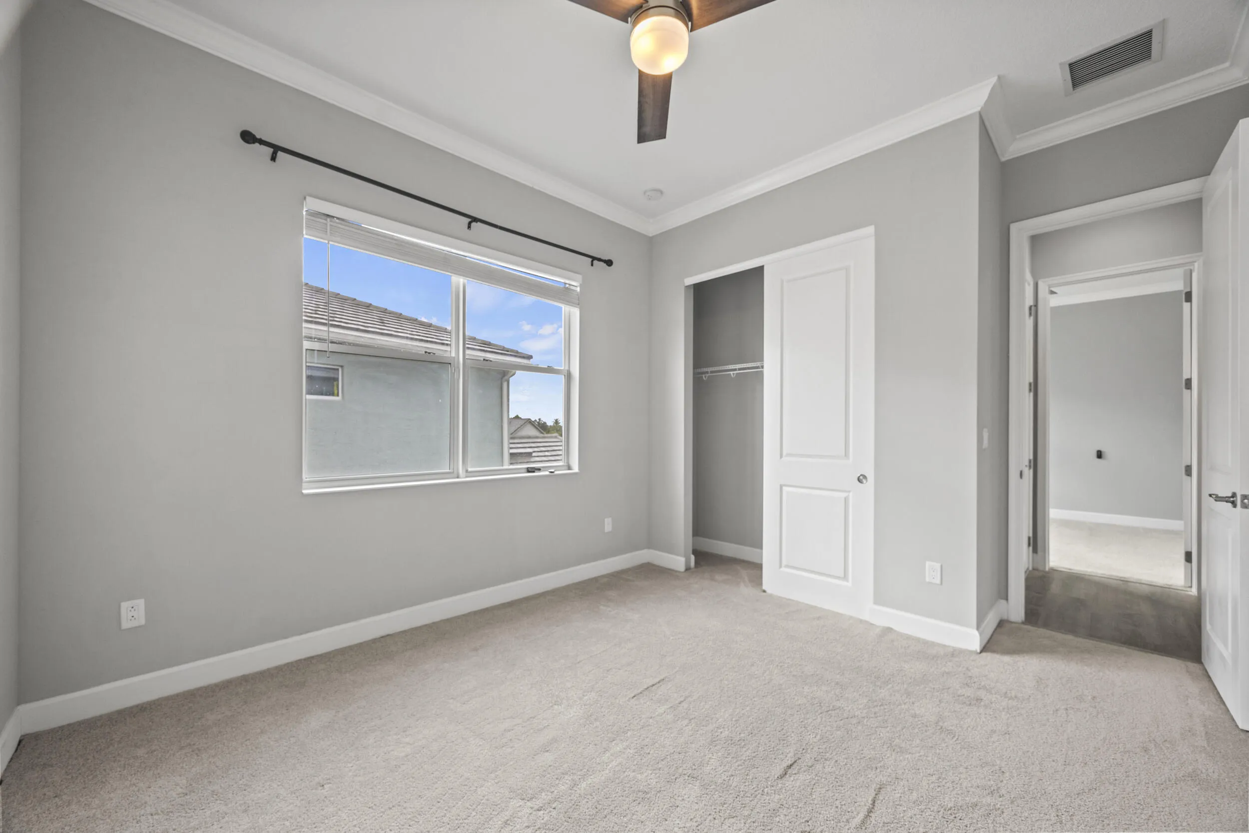 Carpeted room with a ceiling fan, crown molding, double-paned window, and a sliding closet door