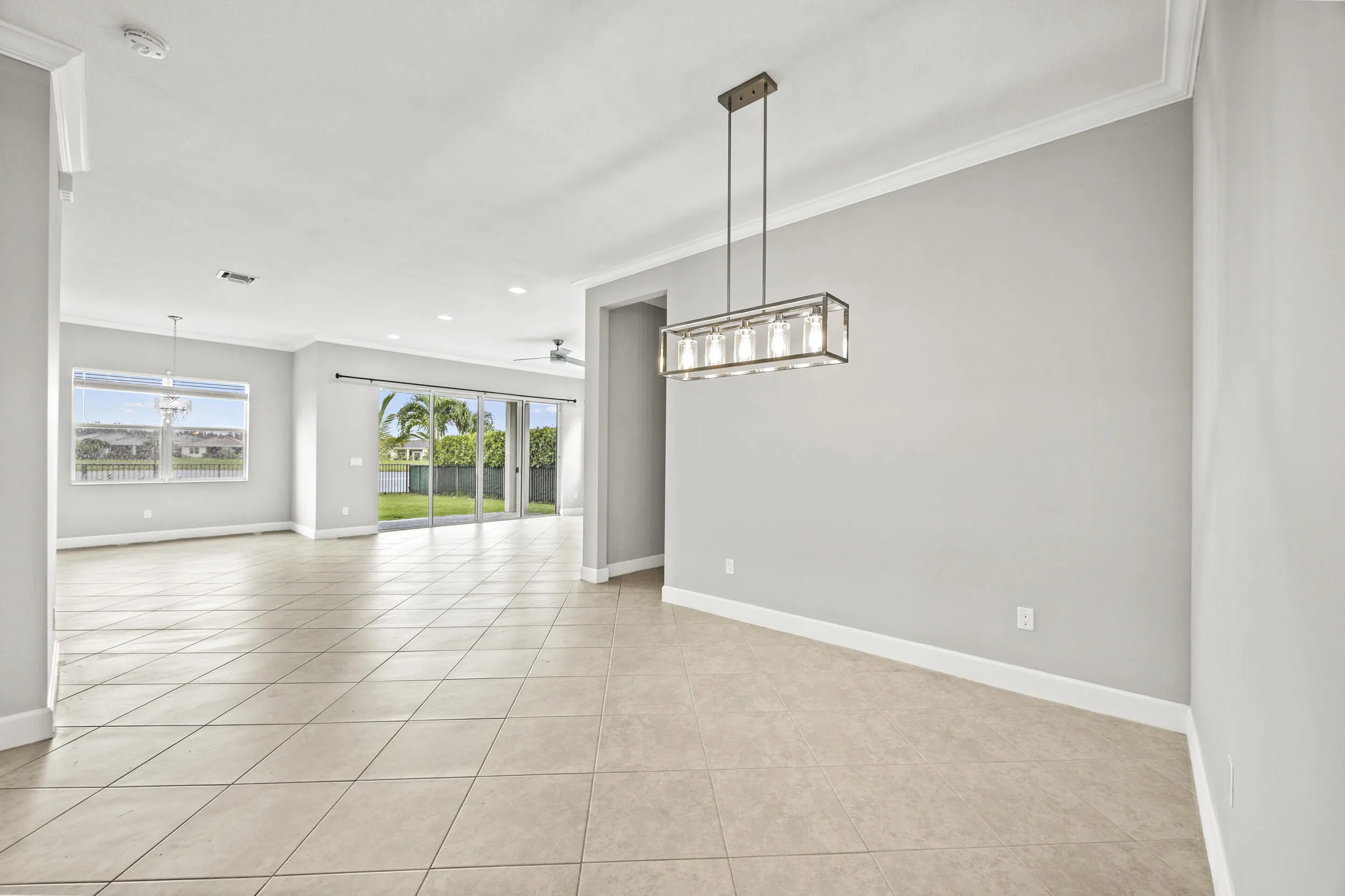 Open-concept interior featuring tile flooring, crown molding, a modern linear chandelier, and sliding glass doors opening to a backyard with water access