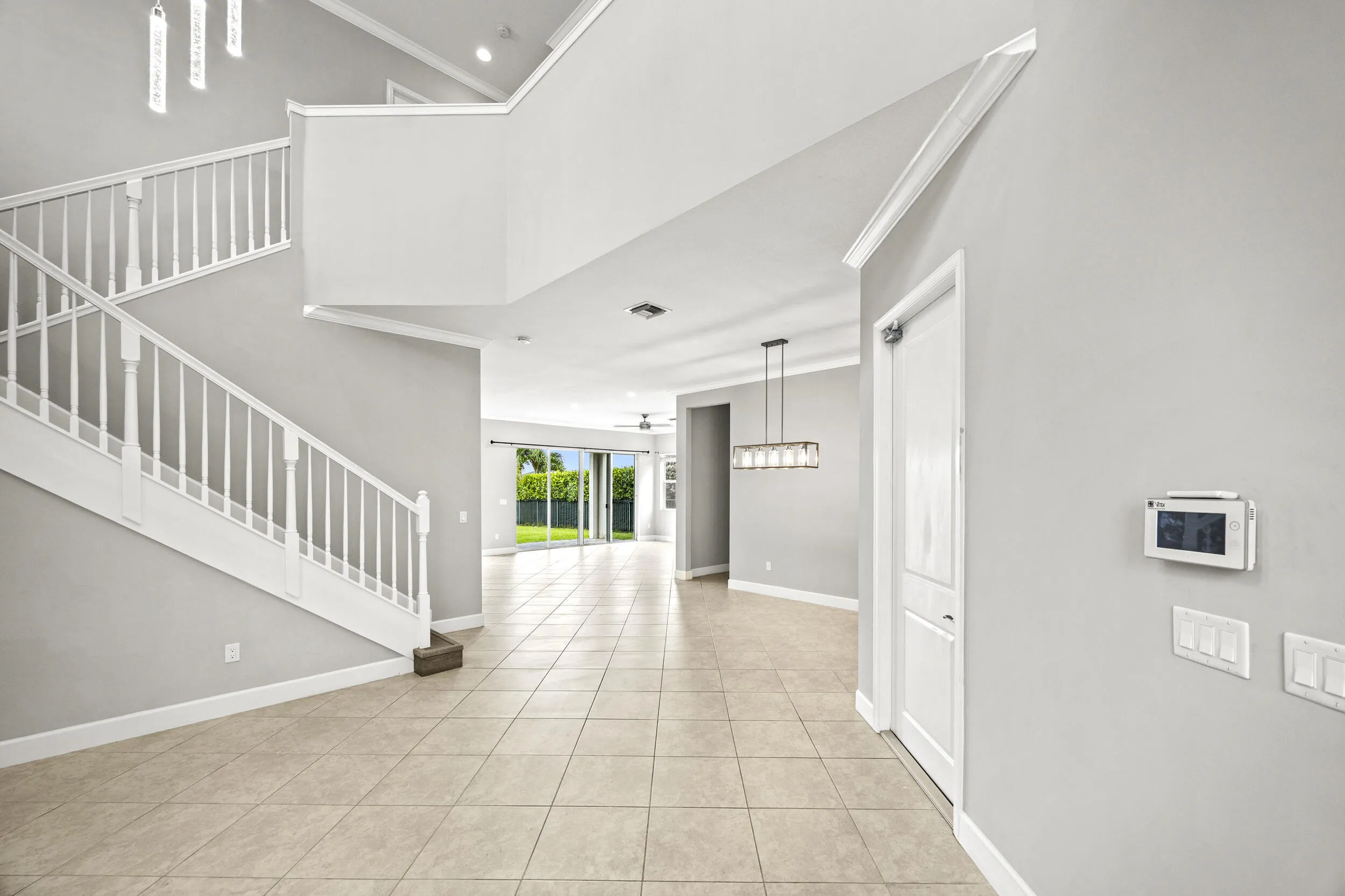 Two-story foyer with a grand staircase, tile flooring, crown molding, and a modern chandelier