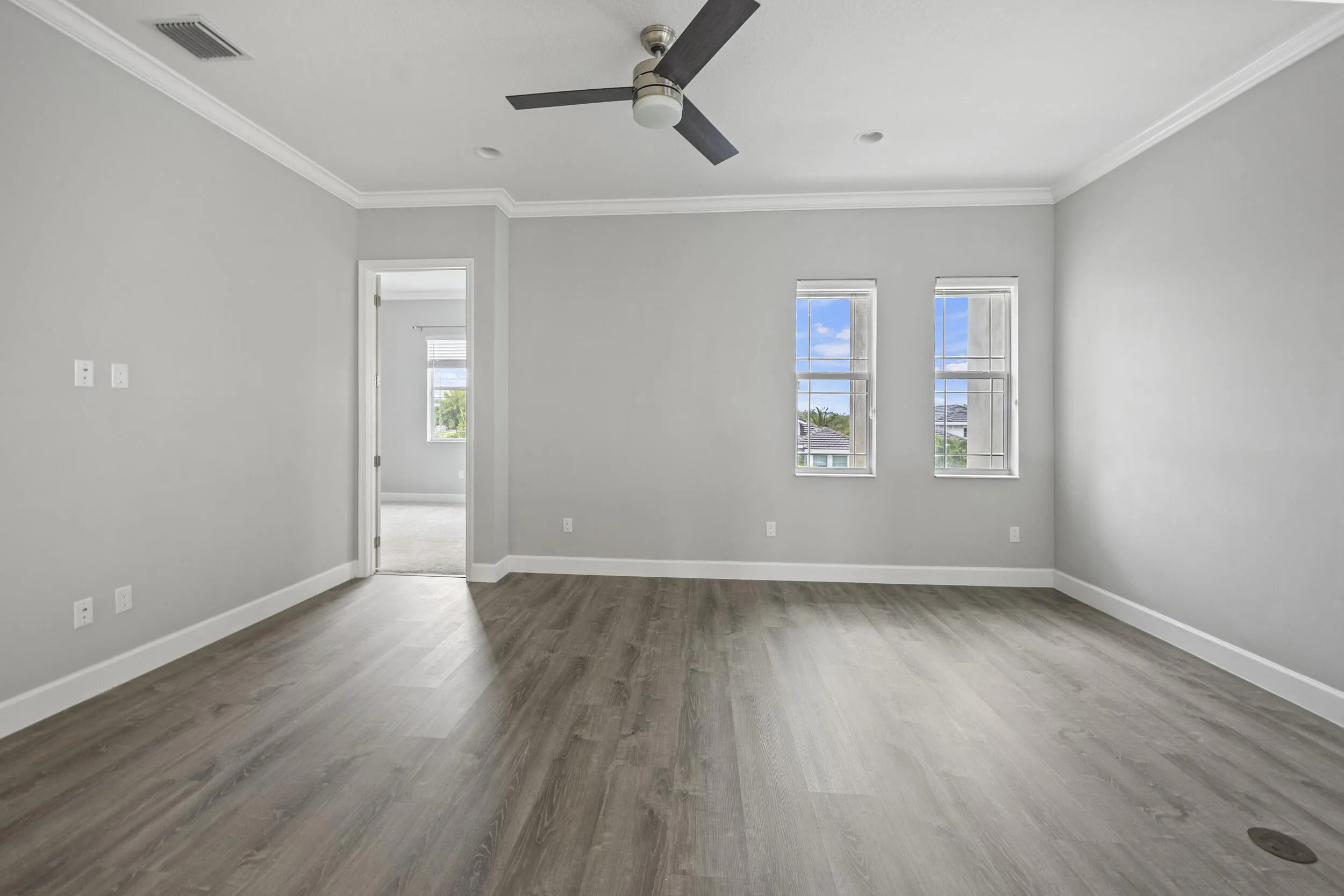 Spacious room featuring wood-finish flooring, light gray wall paint, white crown molding, and an attached ceiling fan