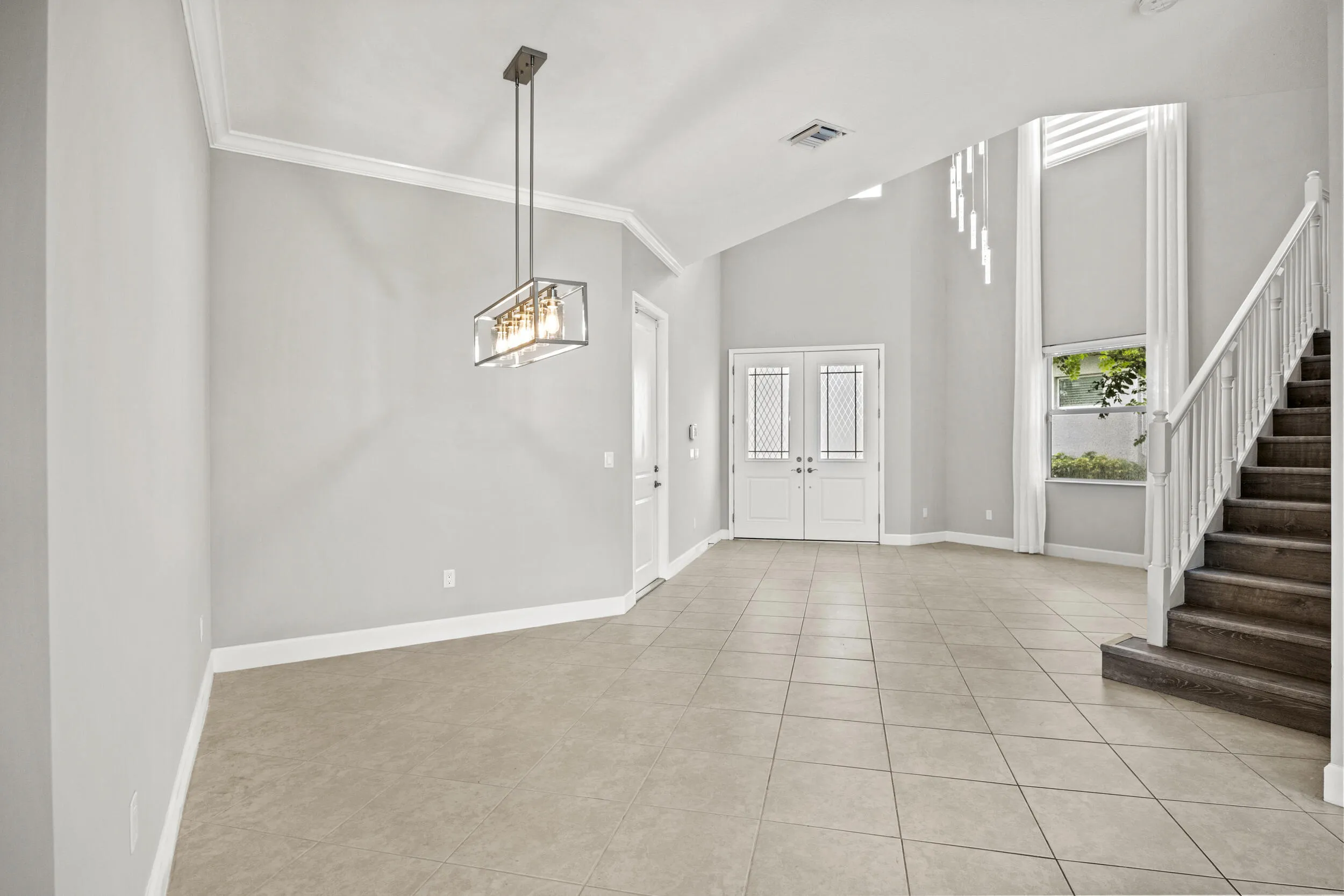 Expansive foyer with vaulted ceilings, tile flooring, a modern linear chandelier, and a prominent staircase with wood-finish treads