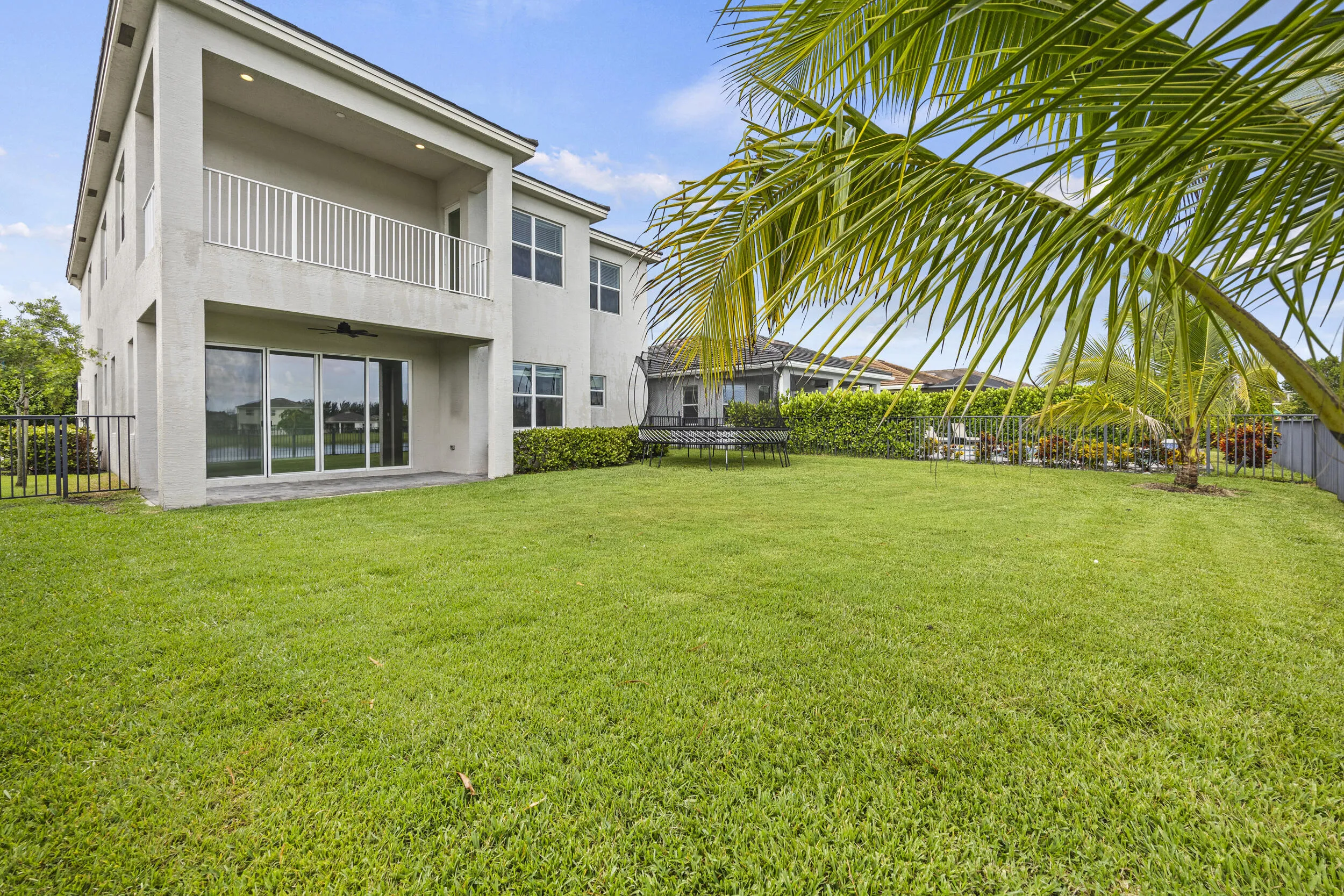 Expansive rear lawn, covered patio, second-story balcony with white railings, and large sliding glass doors