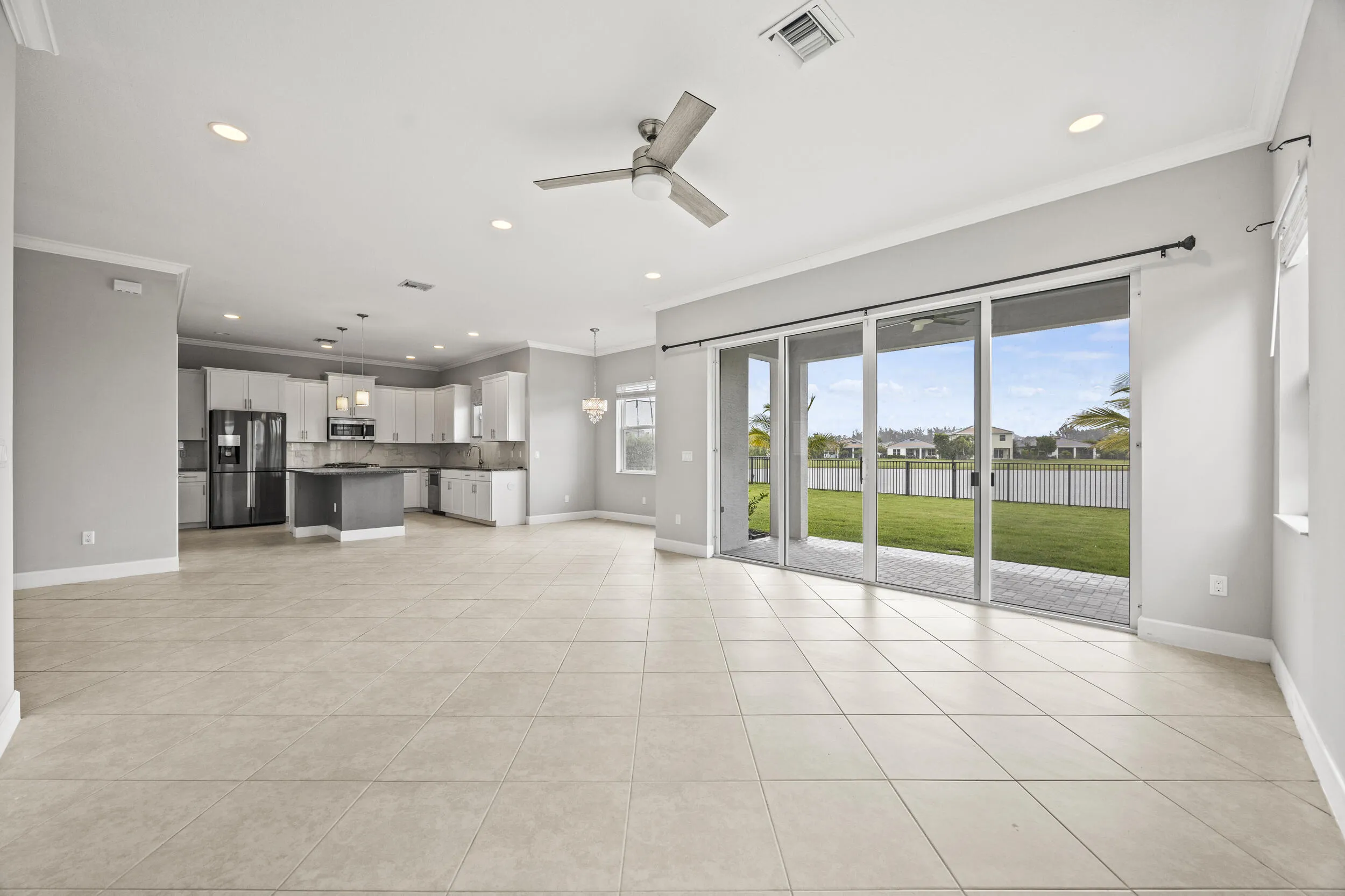Open-concept living space featuring tiled flooring, a modern kitchen with a central island, and sliding glass doors leading to a paved patio