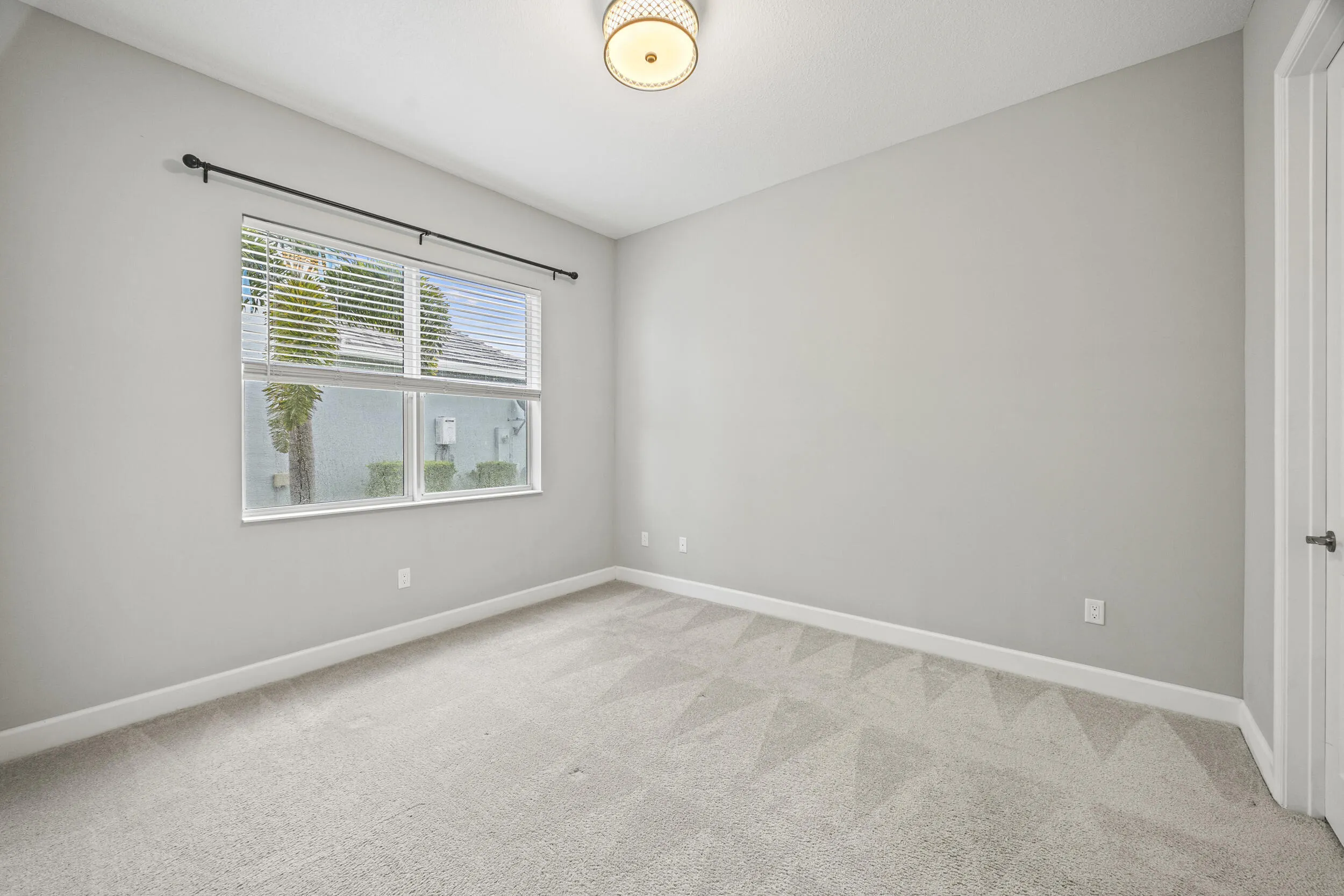 Neutral-toned carpeting, ample window with blinds, ceiling-mounted light fixture, and a white interior door with dark hardware