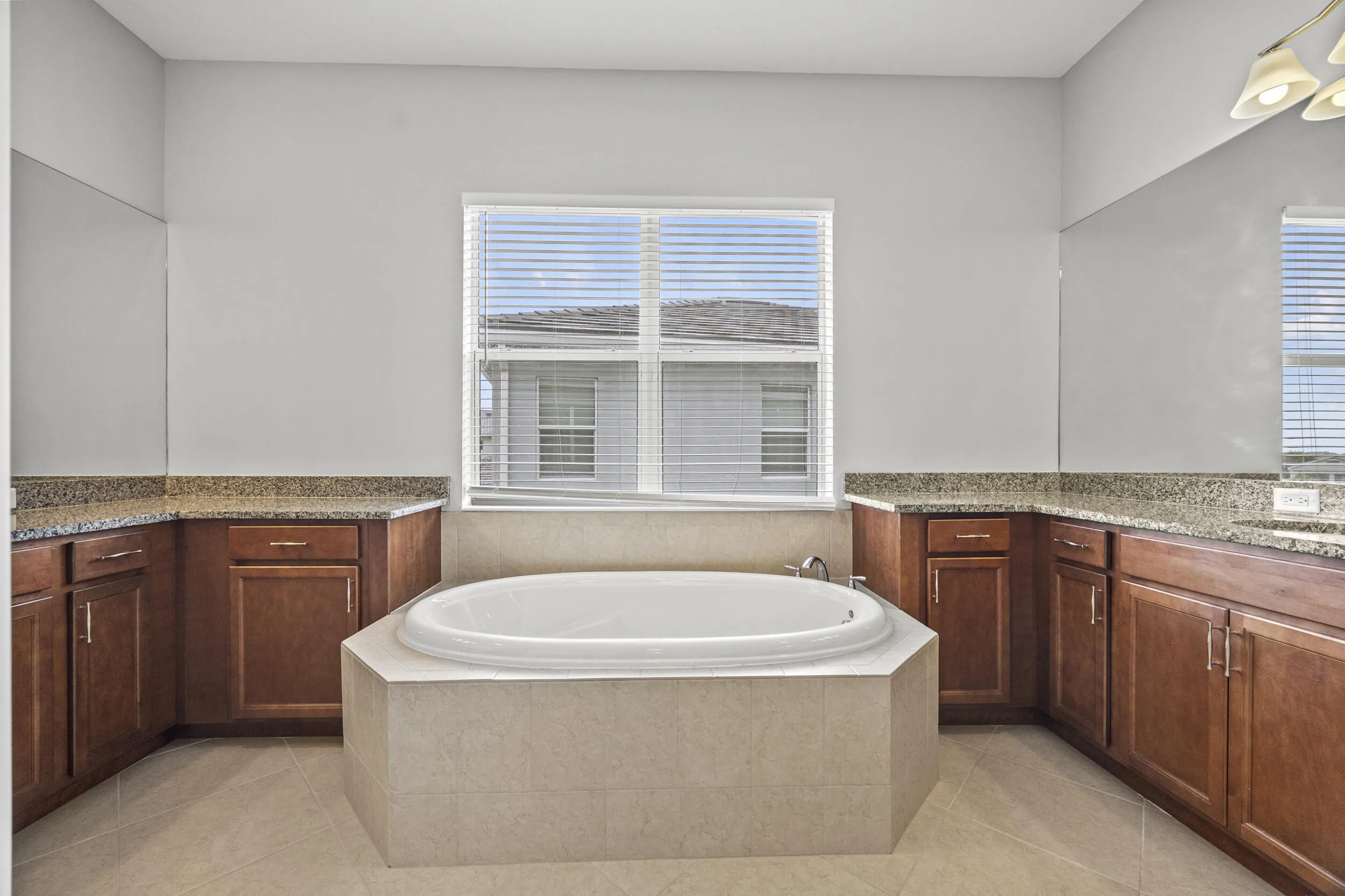 Built-in soaking tub with tiled surround, dual wood-finish vanity cabinets, and speckled countertops