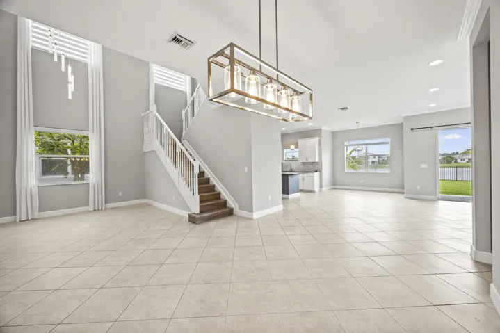 Expansive open-concept living area featuring large format tile flooring, a prominent staircase with wood-finish treads, and a modern linear chandelier