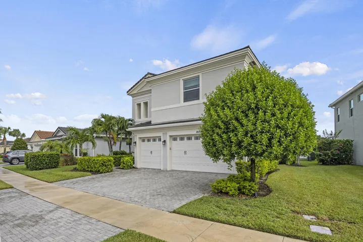 Two-story exterior with a two-car garage, paver driveway, and mature landscaping