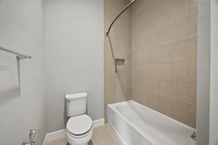 Bathtub with integrated shower, tiled walls, recessed shower niche, and floor-mounted toilet