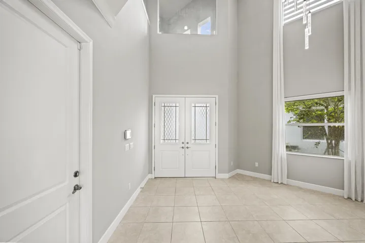 Grand entry with double front doors featuring decorative glass inserts, soaring ceilings, and a tall window