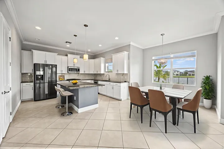 Open-concept kitchen and dining area featuring white cabinetry, stainless steel appliances including a French-door refrigerator, a center island with seating, tile flooring throughout, recessed lighting, and expansive windows showcasing outdoor scenery