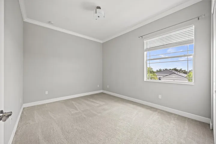 Neutral wall color, crown molding, light-colored carpeting, and a window with horizontal blinds