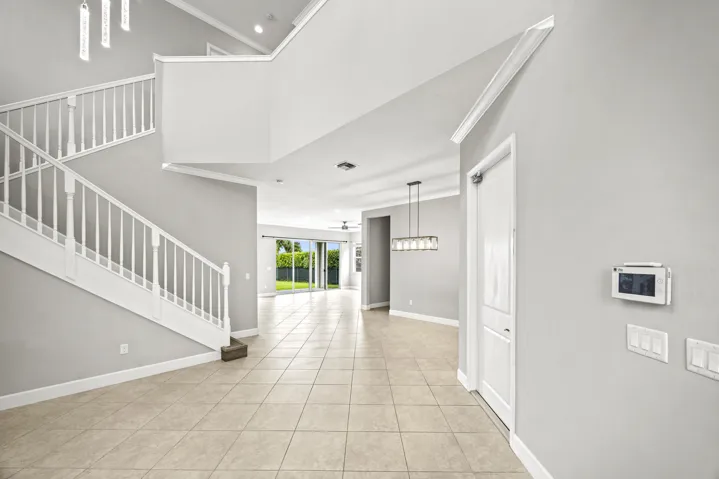 Two-story foyer with a grand staircase, tile flooring, crown molding, and a modern chandelier