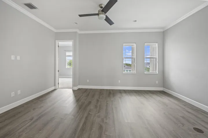 Spacious room featuring wood-finish flooring, light gray wall paint, white crown molding, and an attached ceiling fan