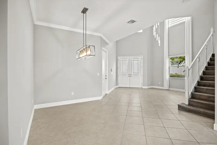 Expansive foyer with vaulted ceilings, tile flooring, a modern linear chandelier, and a prominent staircase with wood-finish treads