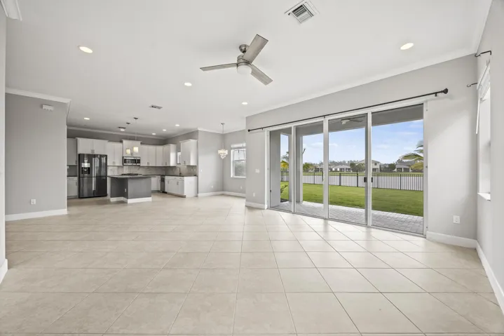 Open-concept living space featuring tiled flooring, a modern kitchen with a central island, and sliding glass doors leading to a paved patio