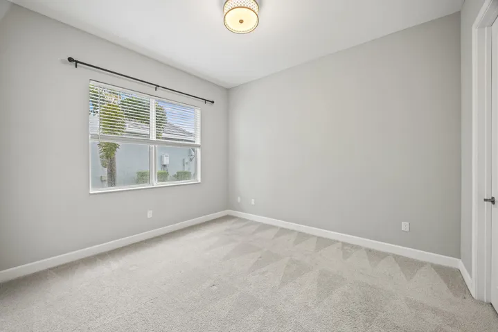 Neutral-toned carpeting, ample window with blinds, ceiling-mounted light fixture, and a white interior door with dark hardware