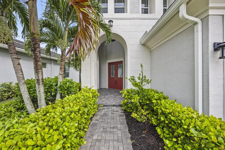 Paver walkway leading to an arched entry with a red double door, surrounded by established landscaping