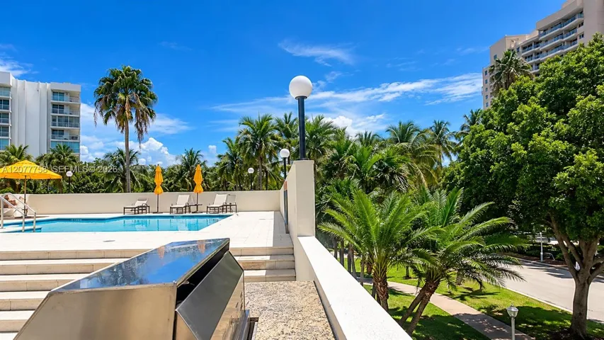 Outdoor swimming pool surrounded by a paved deck, mature palm trees, and lush landscaping
