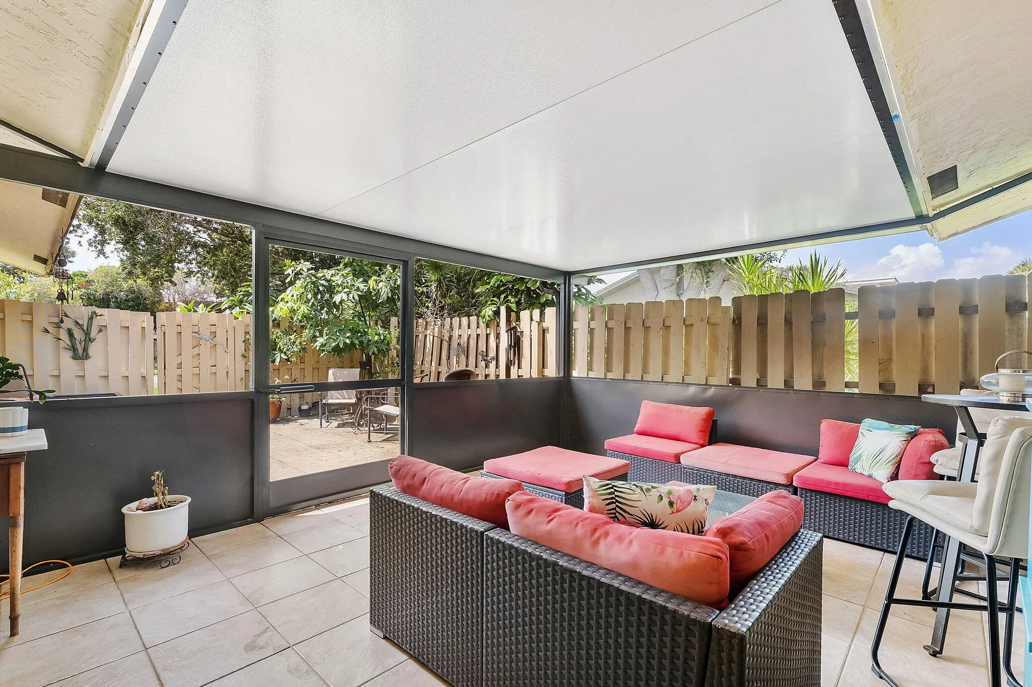 Covered outdoor entertaining space featuring a retractable pergola roof system, tile flooring, panoramic glass panels with partial privacy screening, and integrated seating with cushioning