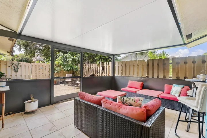 Covered outdoor entertaining space featuring a retractable pergola roof system, tile flooring, panoramic glass panels with partial privacy screening, and integrated seating with cushioning
