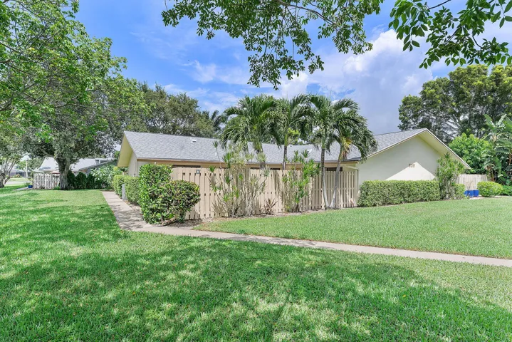 Sprawling grounds featuring mature palm trees and lush landscaping, anchored by a single-story residence with a pitched roof and wood-finish fencing