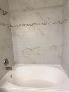 Spa-inspired bathroom featuring a deep soaking tub with curved edges, marble-look tile surround with decorative mosaic accent band, and polished chrome fixtures