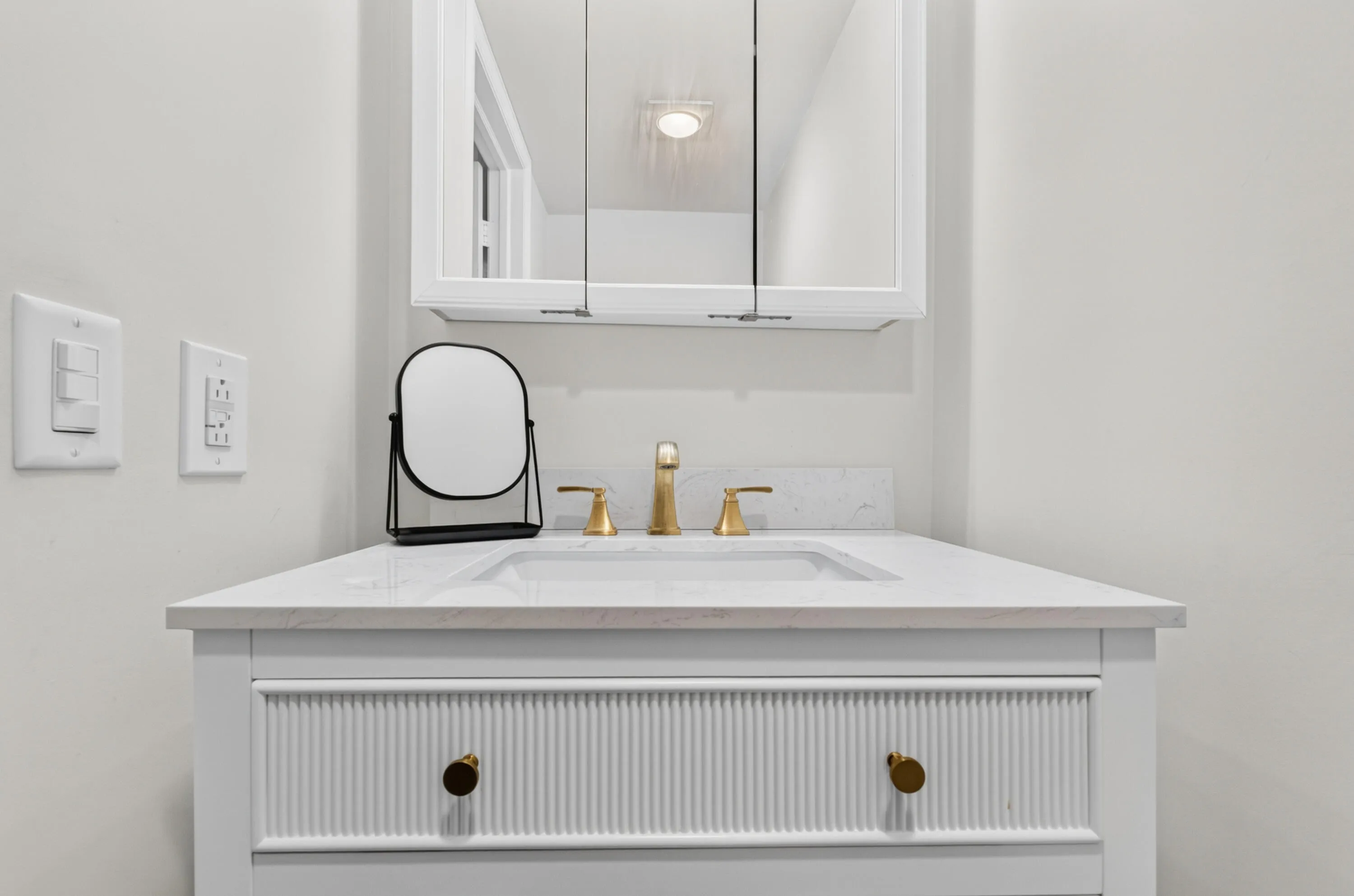 Elegant bathroom vanity featuring a white ribbed cabinetry base with brass hardware, a light stone countertop, and a polished brass three-hole faucet