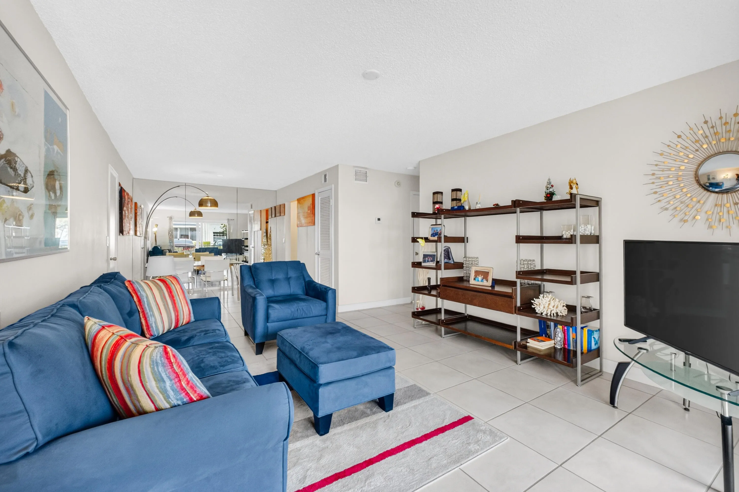 Open-concept living area featuring tile flooring, abundant natural light from multiple windows, built-in shelving with wood-finish frames, and a flat-screen television mounted above a media console