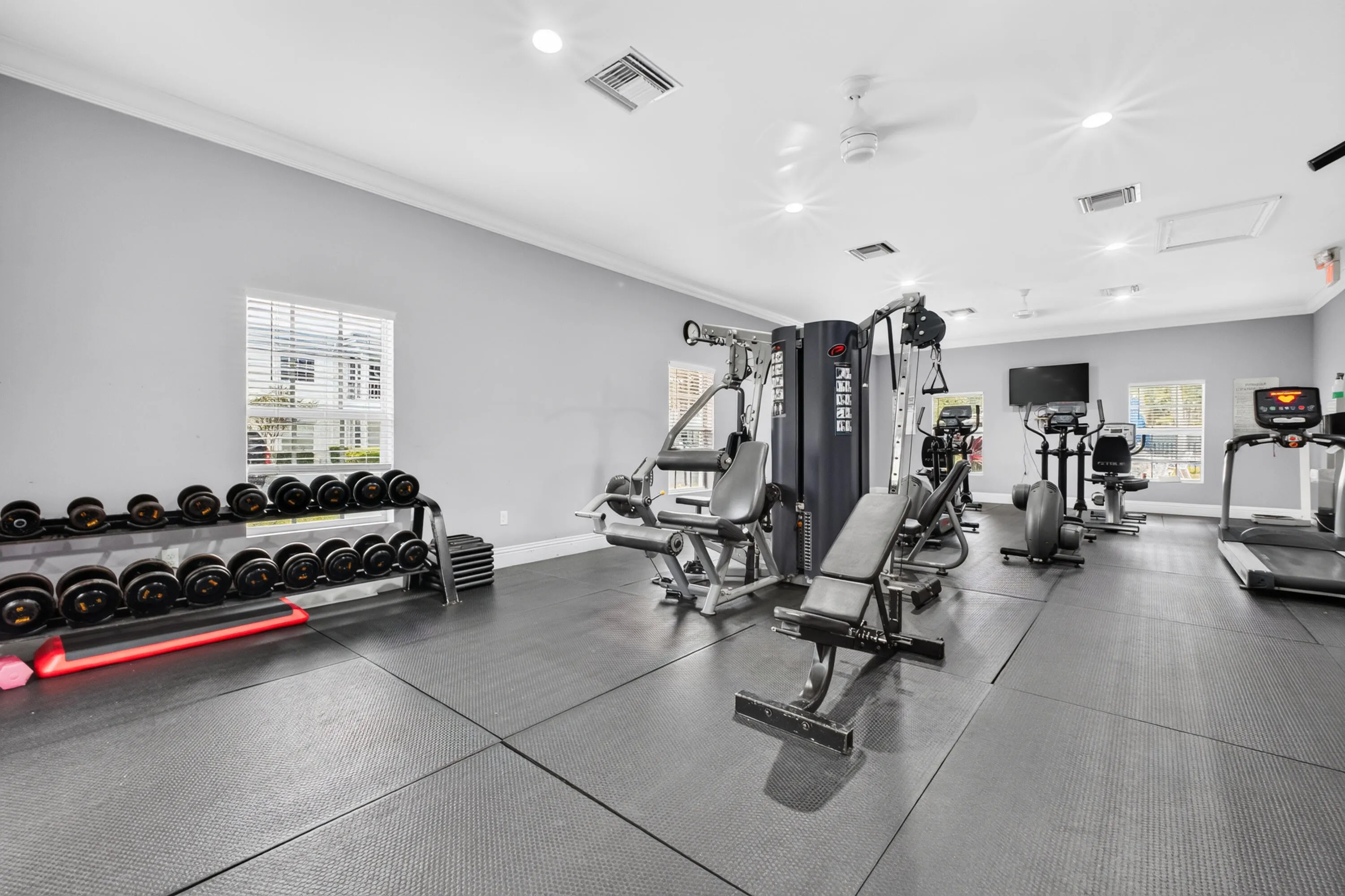 State-of-the-art fitness facility featuring multiple strength training machines, comprehensive dumbbell rack system, rubberized flooring throughout, and abundant natural lighting from large windows