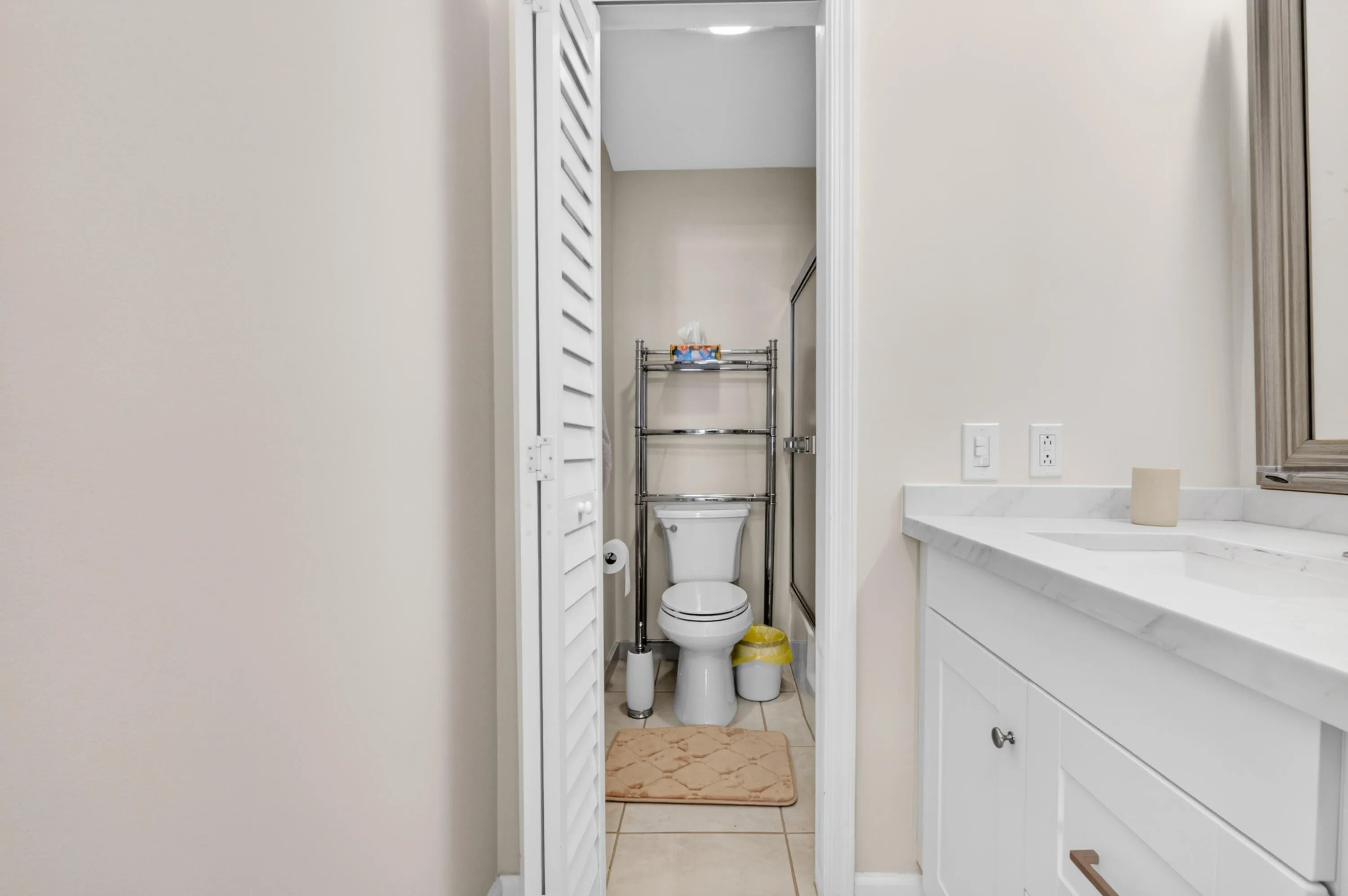 Efficient bathroom layout featuring a marble-topped vanity with integrated sink, white cabinetry, and a separate water closet with tile flooring