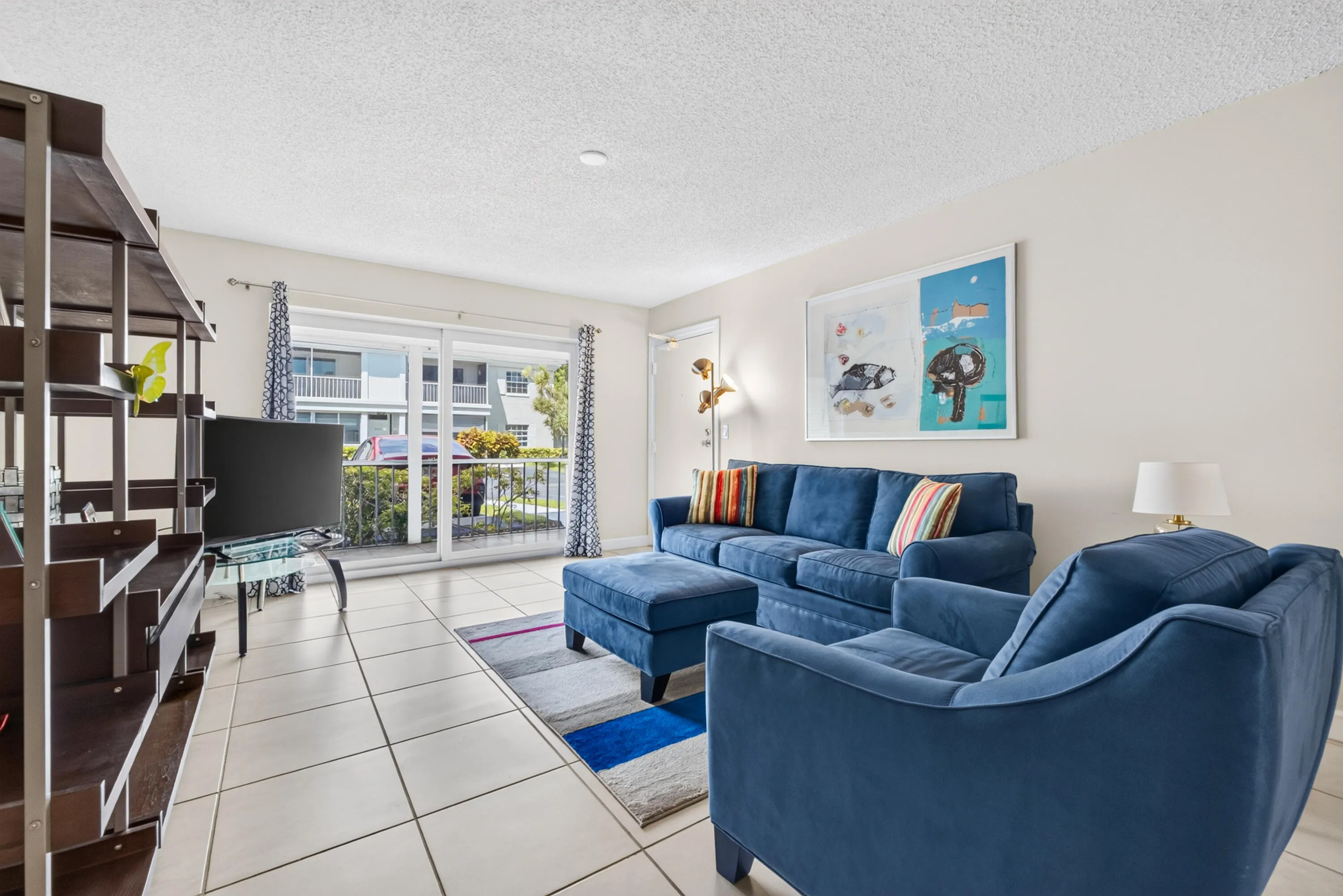 Bright, open living area featuring tile flooring, built-in shelving with dark wood-finish cabinetry, and glass sliding doors opening to a balcony with city views