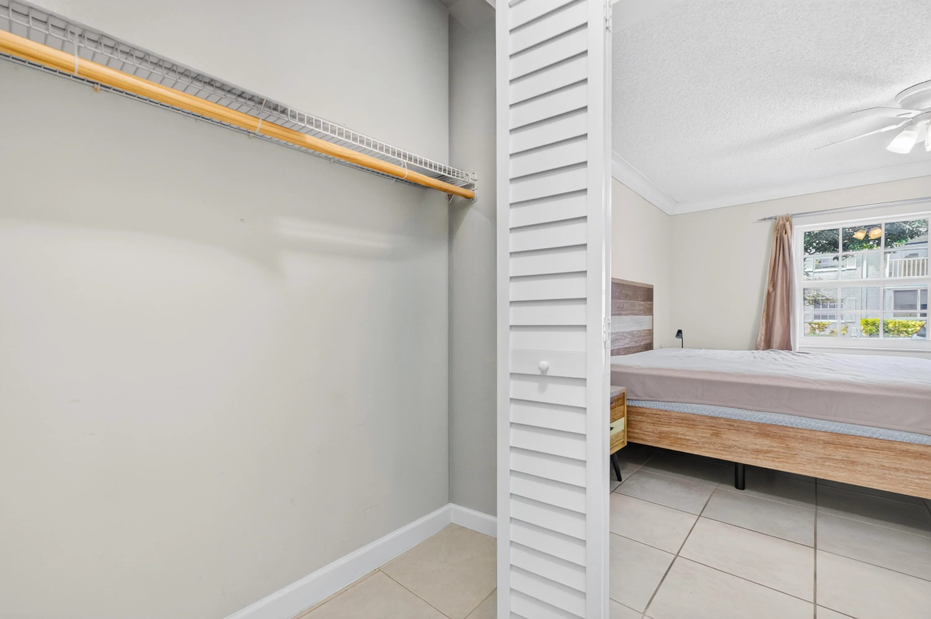 Spacious walk-in closet with dual hanging rods, louvered storage door, and tile flooring