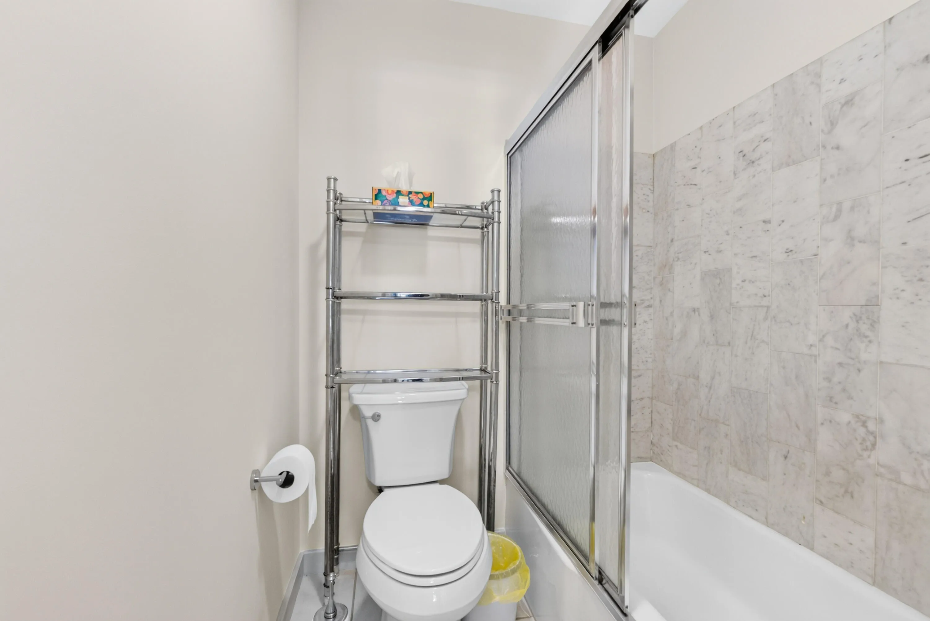White tiled shower surround with a sliding glass door and a white bathtub