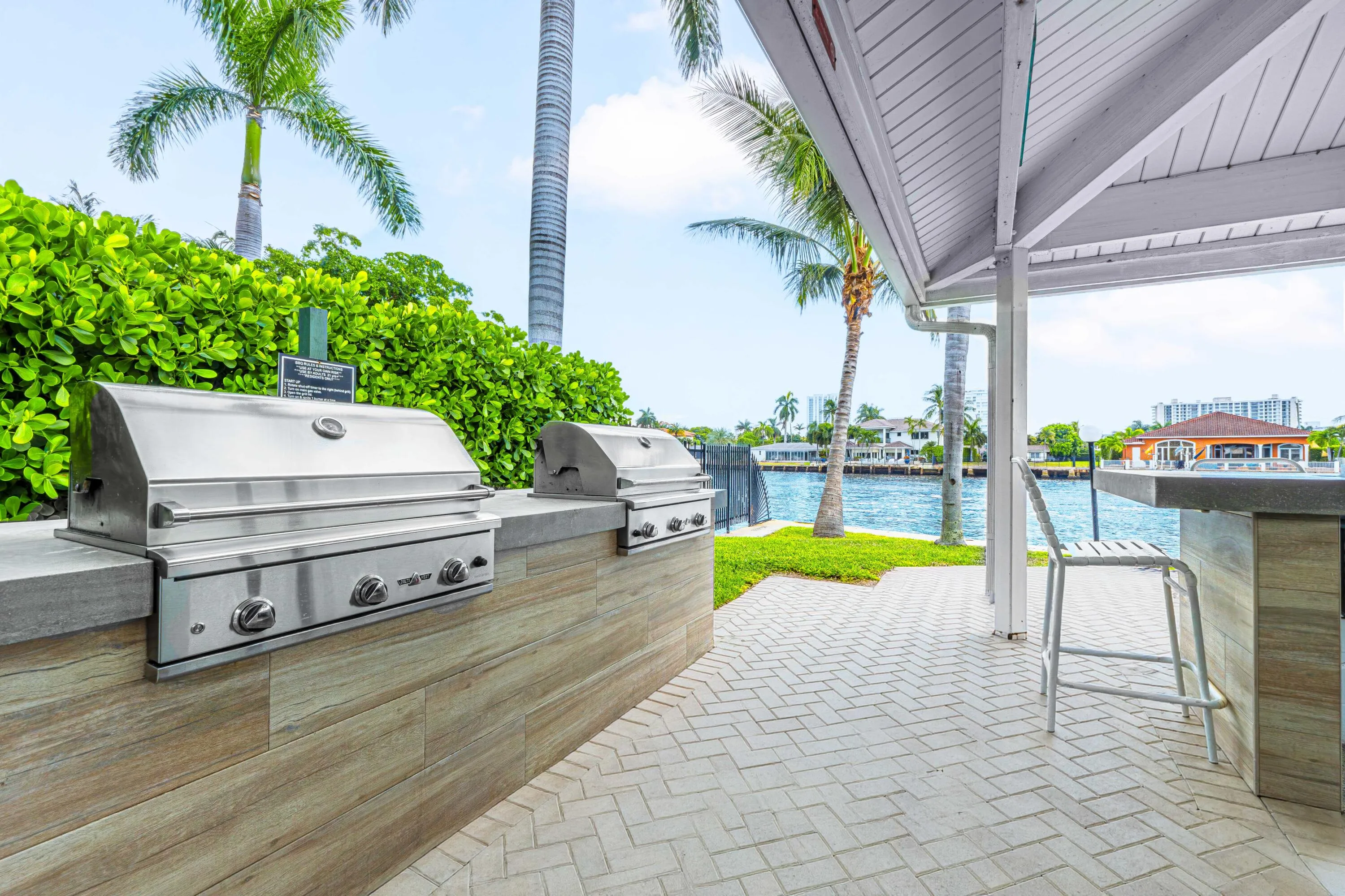 Outdoor kitchen with dual stainless steel grills, a built-in bar, and a covered patio area with herringbone paver flooring
