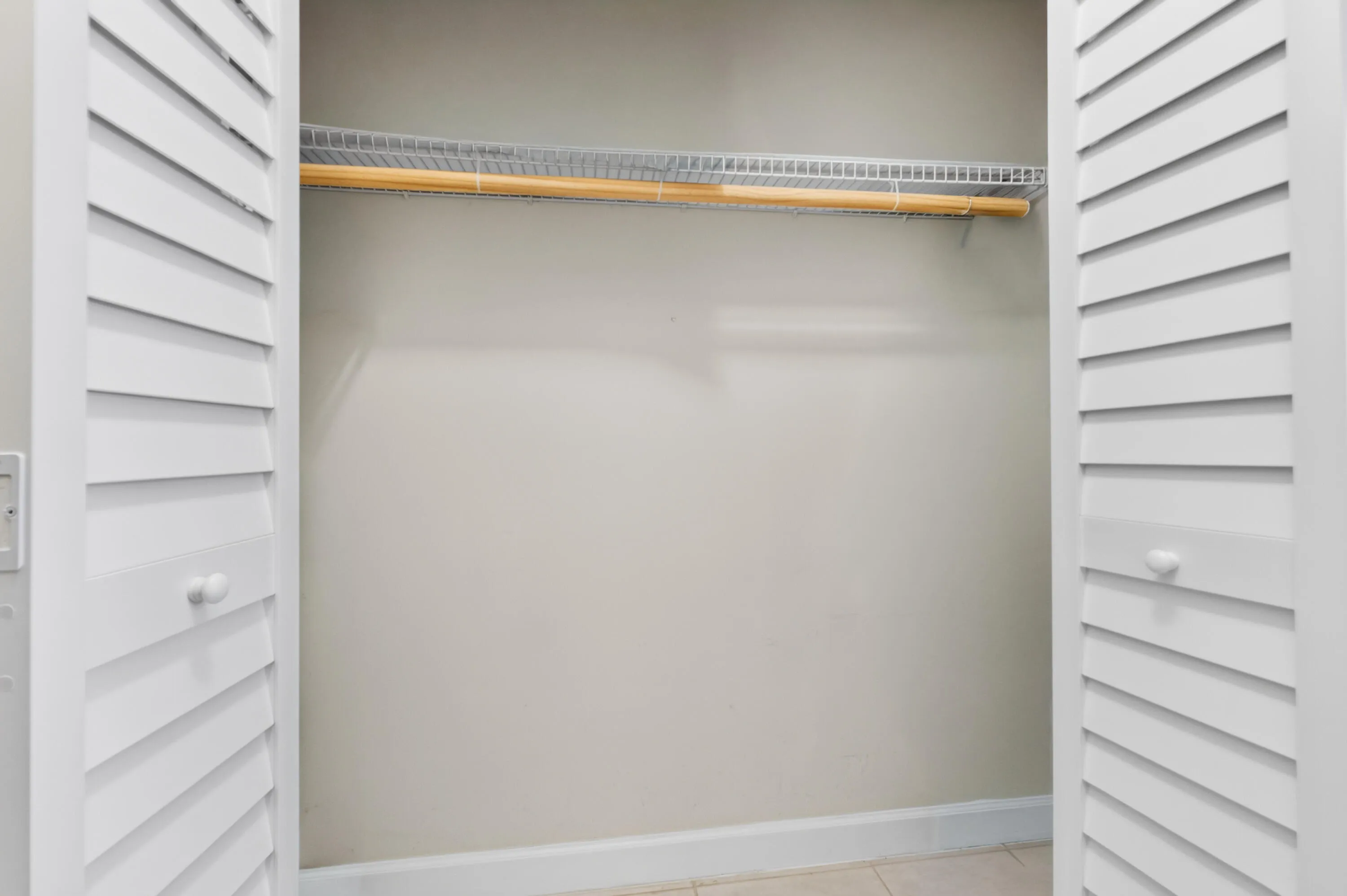 Louvered bi-fold doors opening to a built-in closet system with a wood hanging rod and wire shelving