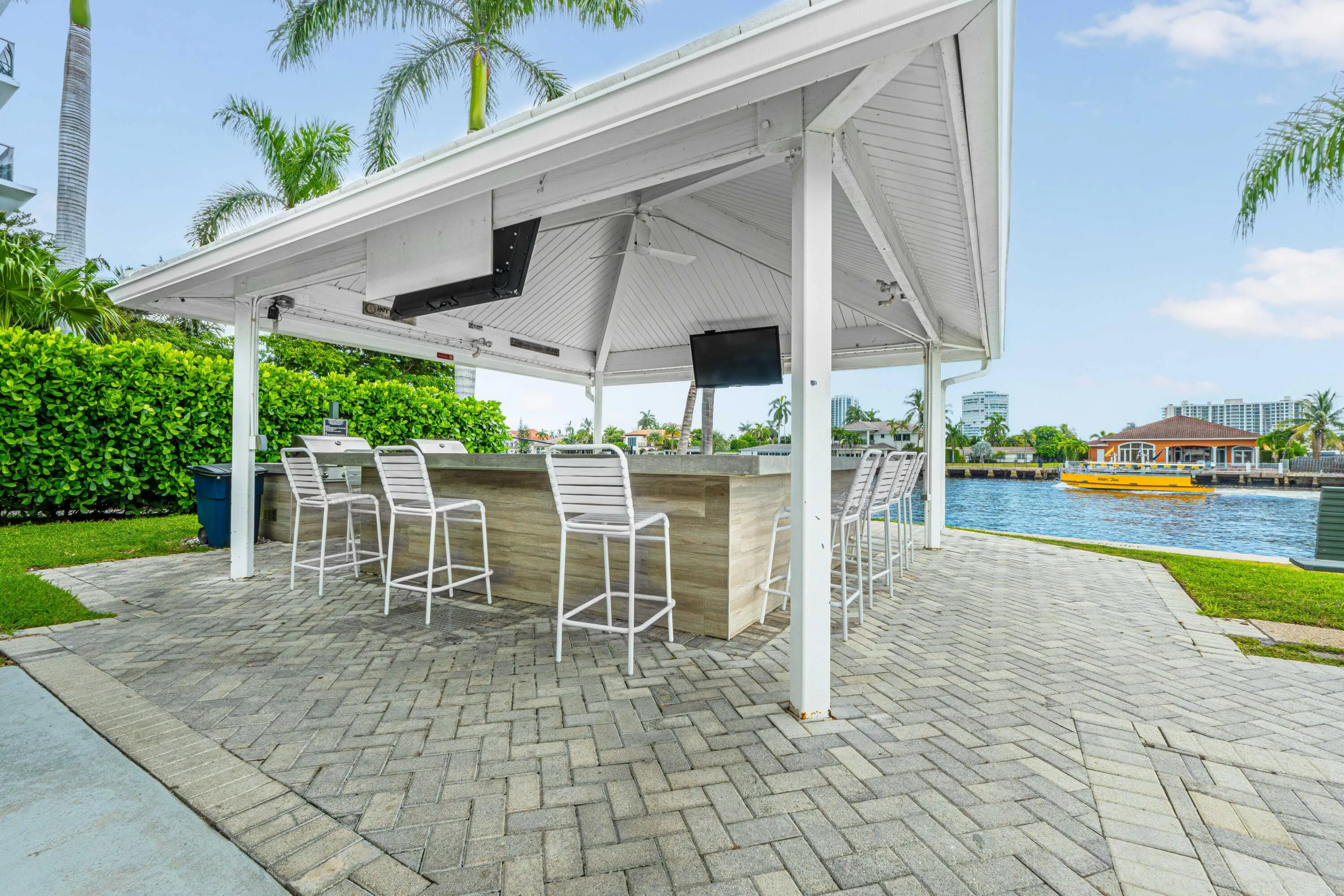Waterfront covered outdoor bar with built-in appliances, herringbone paver patio, and lush landscaping