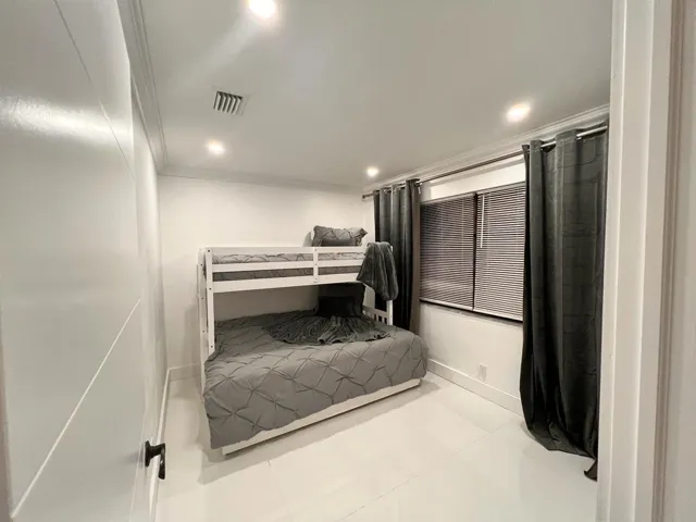 Recessed lighting illuminates the room, featuring crown molding, a window with blinds, and white tile flooring