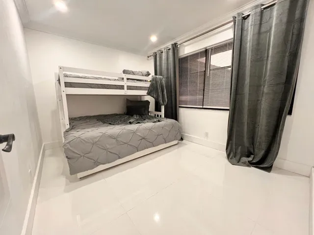 Recessed lighting illuminates a room featuring white walls and white tiled flooring