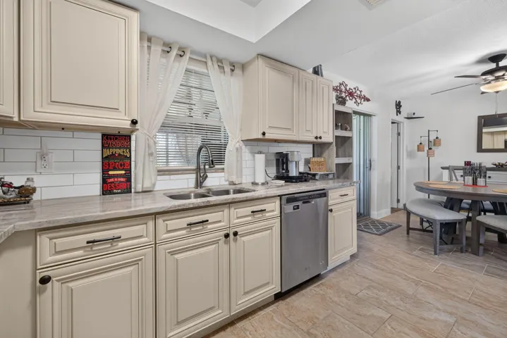 Kitchen featuring light-toned cabinetry, light-toned countertops, a stainless steel dishwasher, a subway tile backsplash, and wood-finish tile flooring
