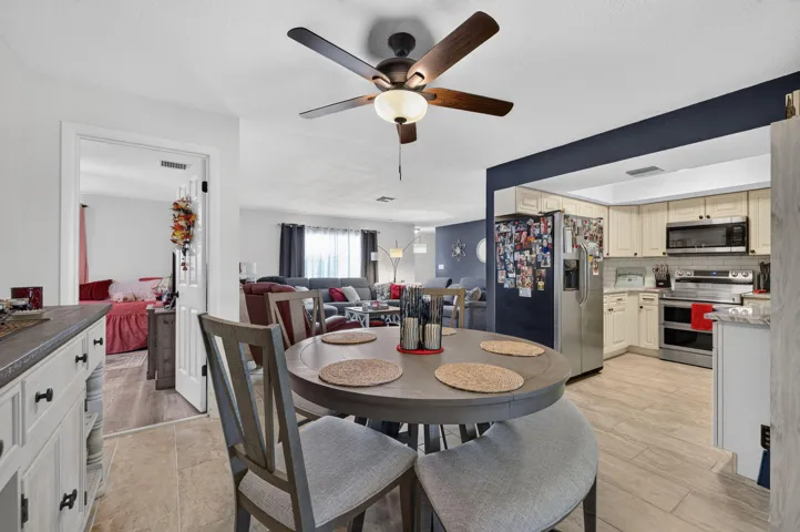 Dining area featuring a ceiling fan with light fixture, adjacent to a kitchen with light-colored cabinetry and stainless steel appliances