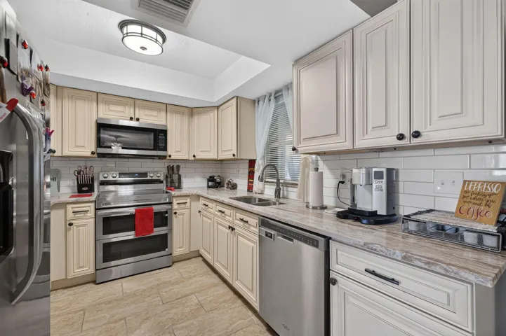 Kitchen featuring neutral cabinetry, stainless steel appliances, a subway tile backsplash, light-toned countertops, and tile flooring