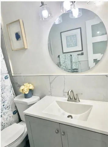 Vanity with a solid surface countertop, integrated basin, brushed metal faucet, large circular wall mirror, and floor-to-ceiling wall tile