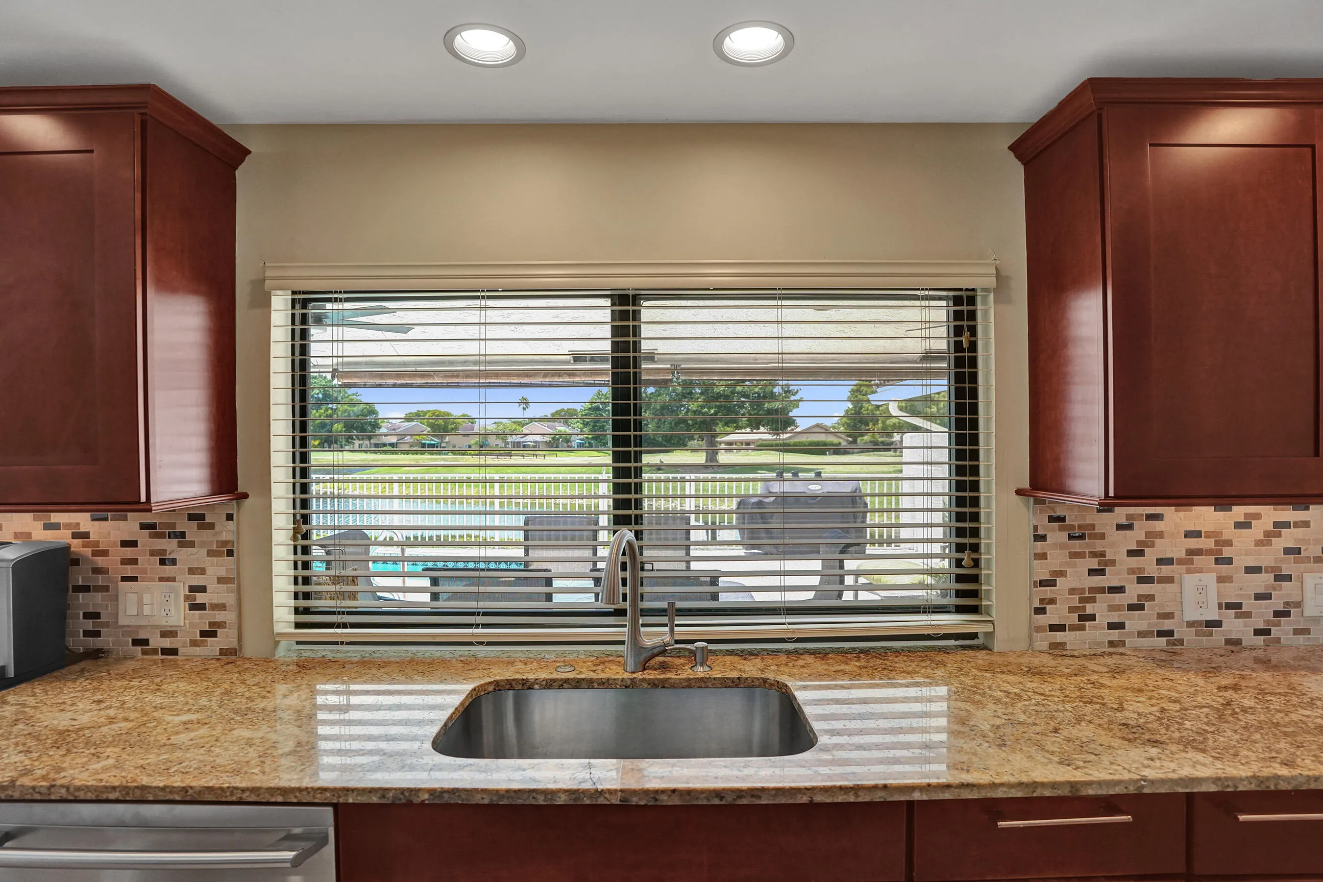 Kitchen featuring a stainless steel undermount sink, granite countertops, mosaic tile backsplash, and dark wood-finish cabinetry