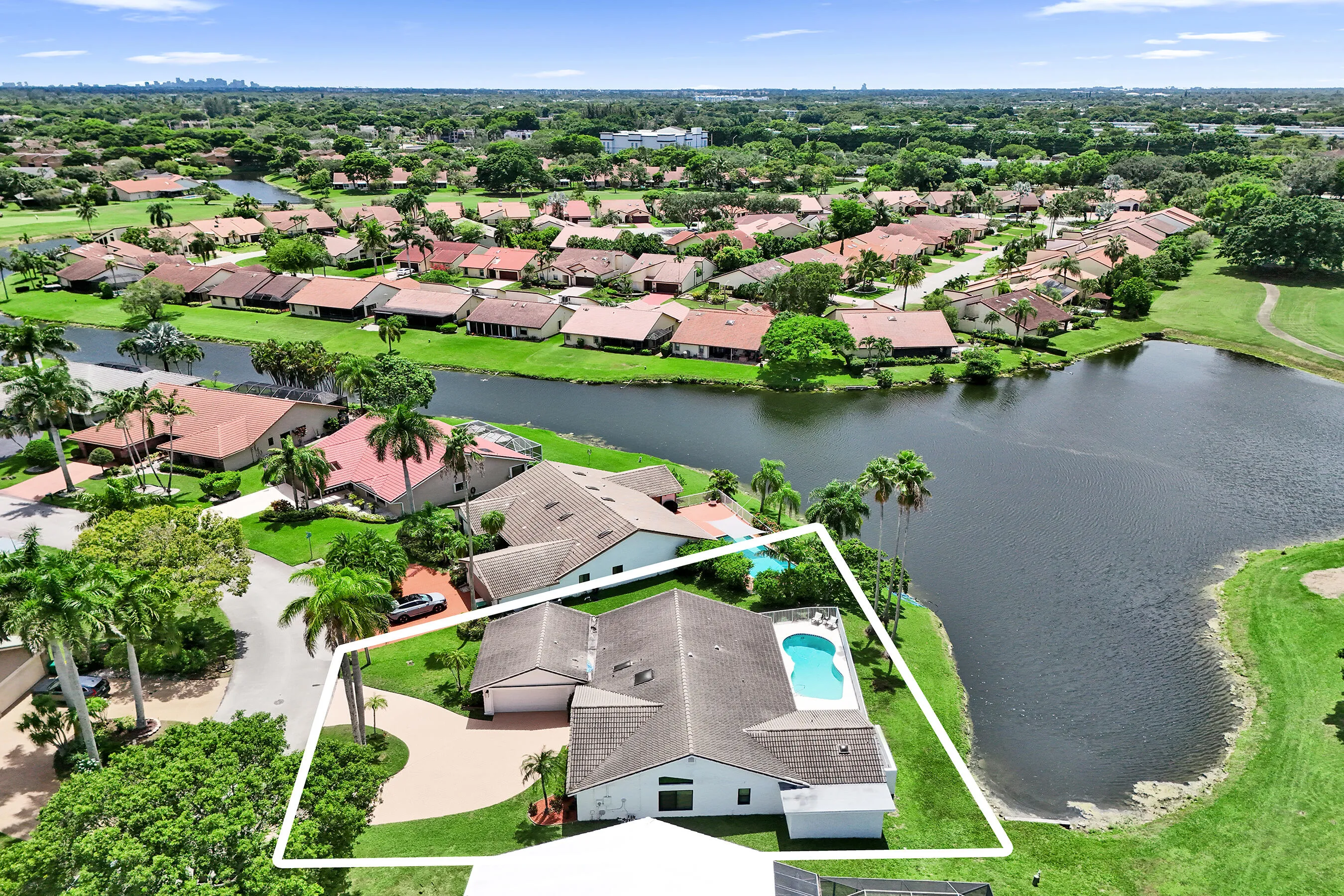 Aerial perspective showcasing a single-story residence with an attached garage, a private swimming pool, and a paved driveway, bordered by a large body of water