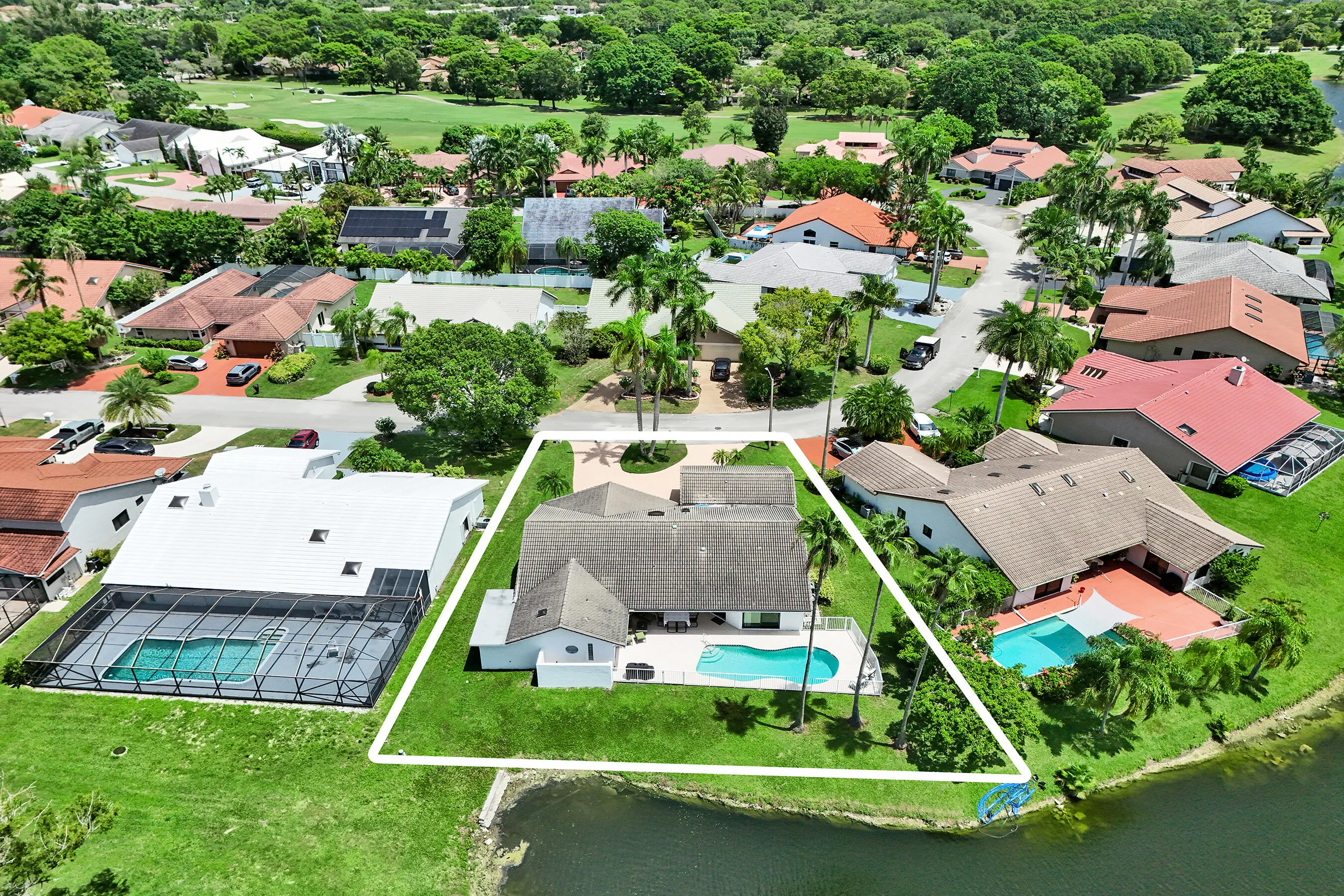 Waterfront property featuring a private swimming pool, expansive patio, mature palm trees, and a well-maintained lawn
