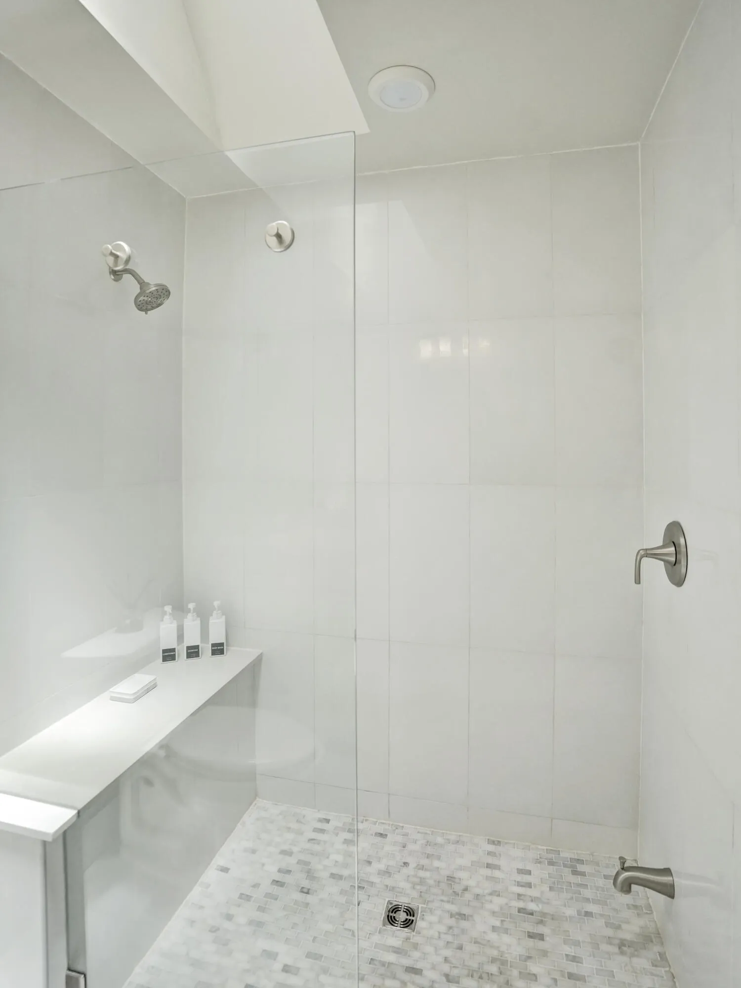 Glass-enclosed shower with white tiled walls, a built-in bench, and a mosaic tile floor