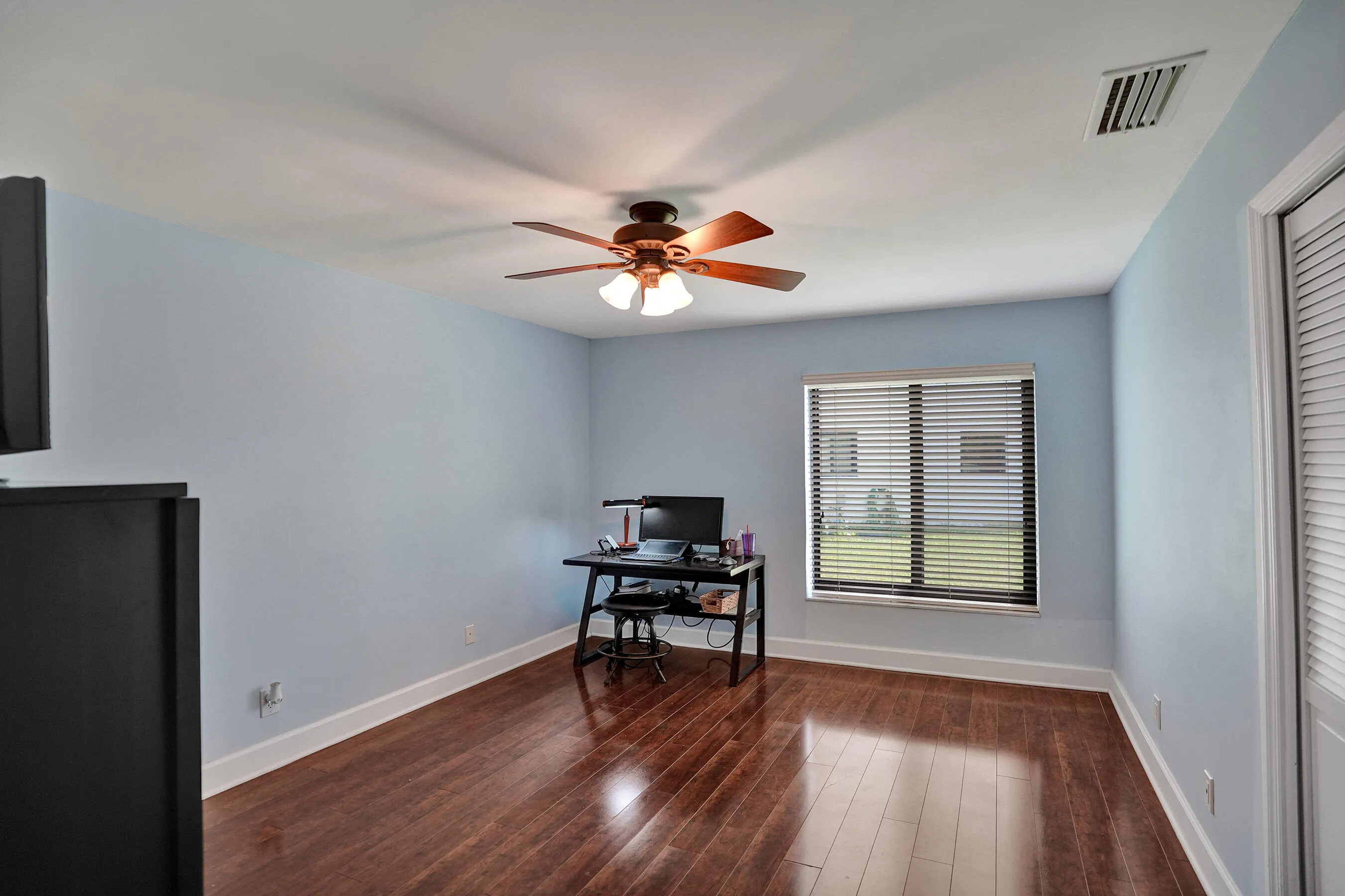 Wood-finish flooring with a flush-mounted ceiling fan and a window with horizontal blinds